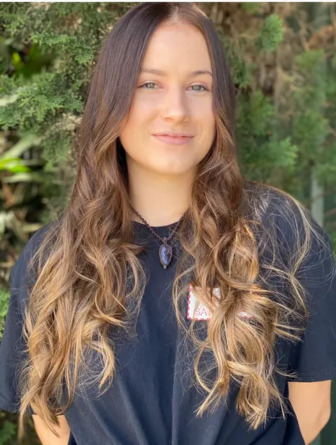 Young woman with long brunette hair and soft caramel balayage waves, garden background