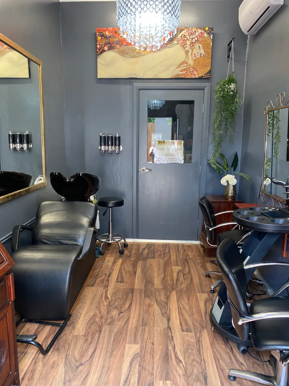 Inside Hair by Ingrid: charcoal walls, a crystal chandelier, gold framed mirrors, black chairs and a timber floor